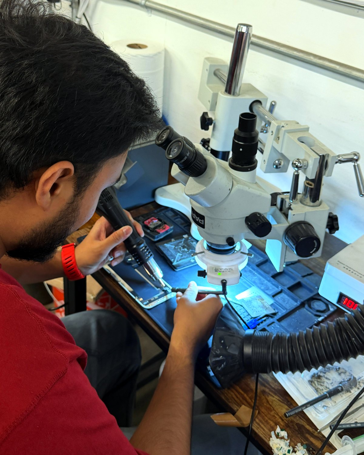 Technician micro-soldering a phone logic board under a microscope